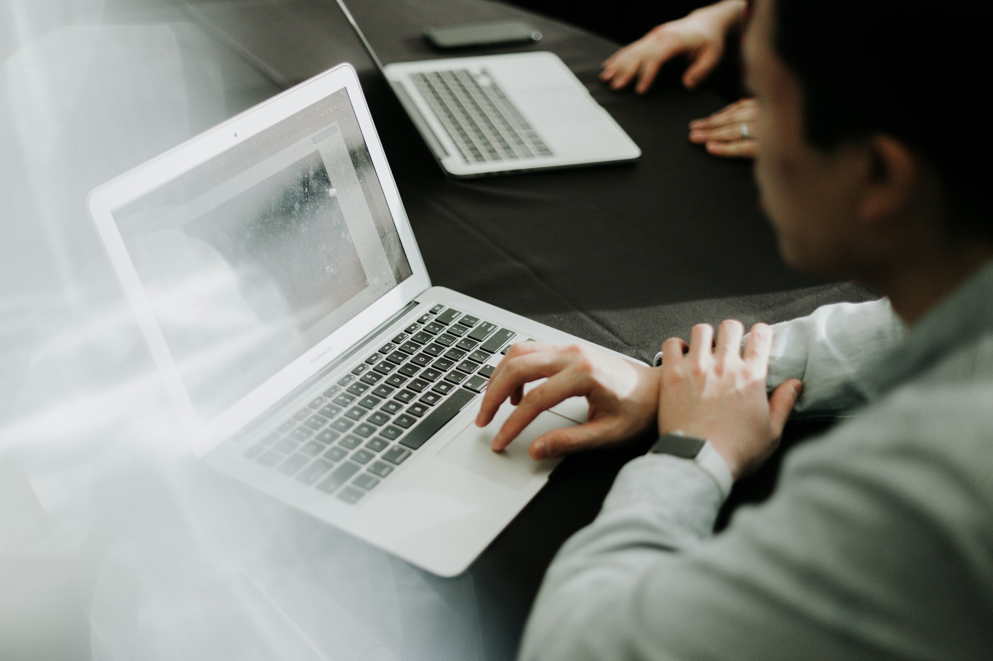A person working at a laptop, a second laptop across the table.